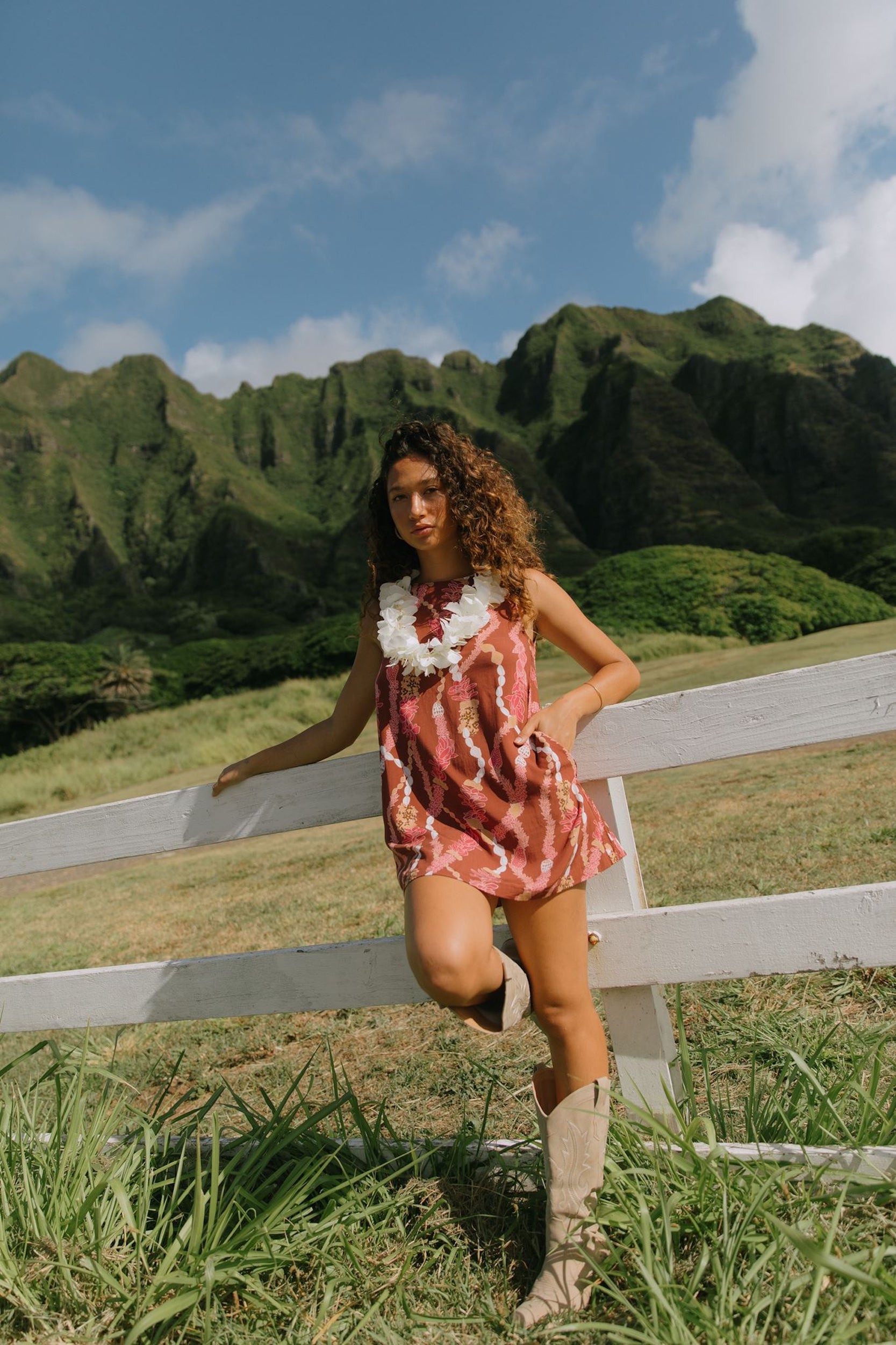 woman with brown hair wearing red-brown high neck scoop back dress with lei print