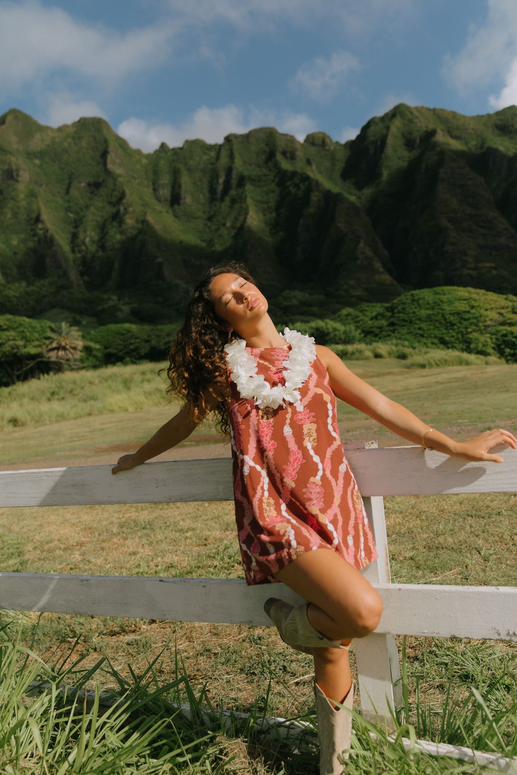 woman with brown hair wearing red-brown high neck scoop back dress with lei print