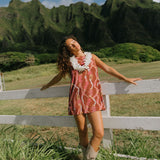 woman with brown hair wearing red-brown high neck scoop back dress with lei print