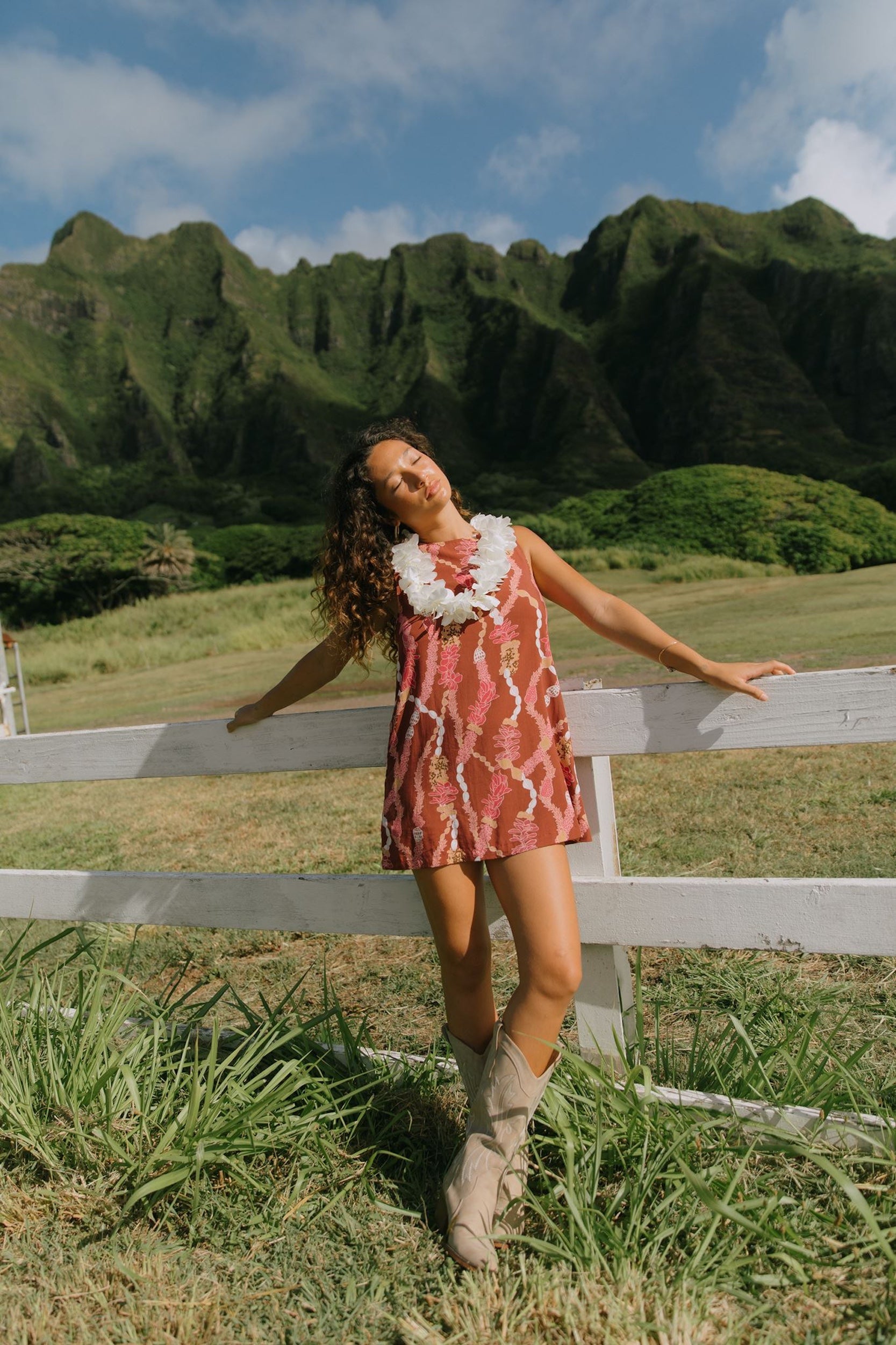 woman with brown hair wearing red-brown high neck scoop back dress with lei print