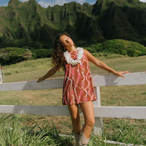 woman with brown hair wearing red-brown high neck scoop back dress with lei print