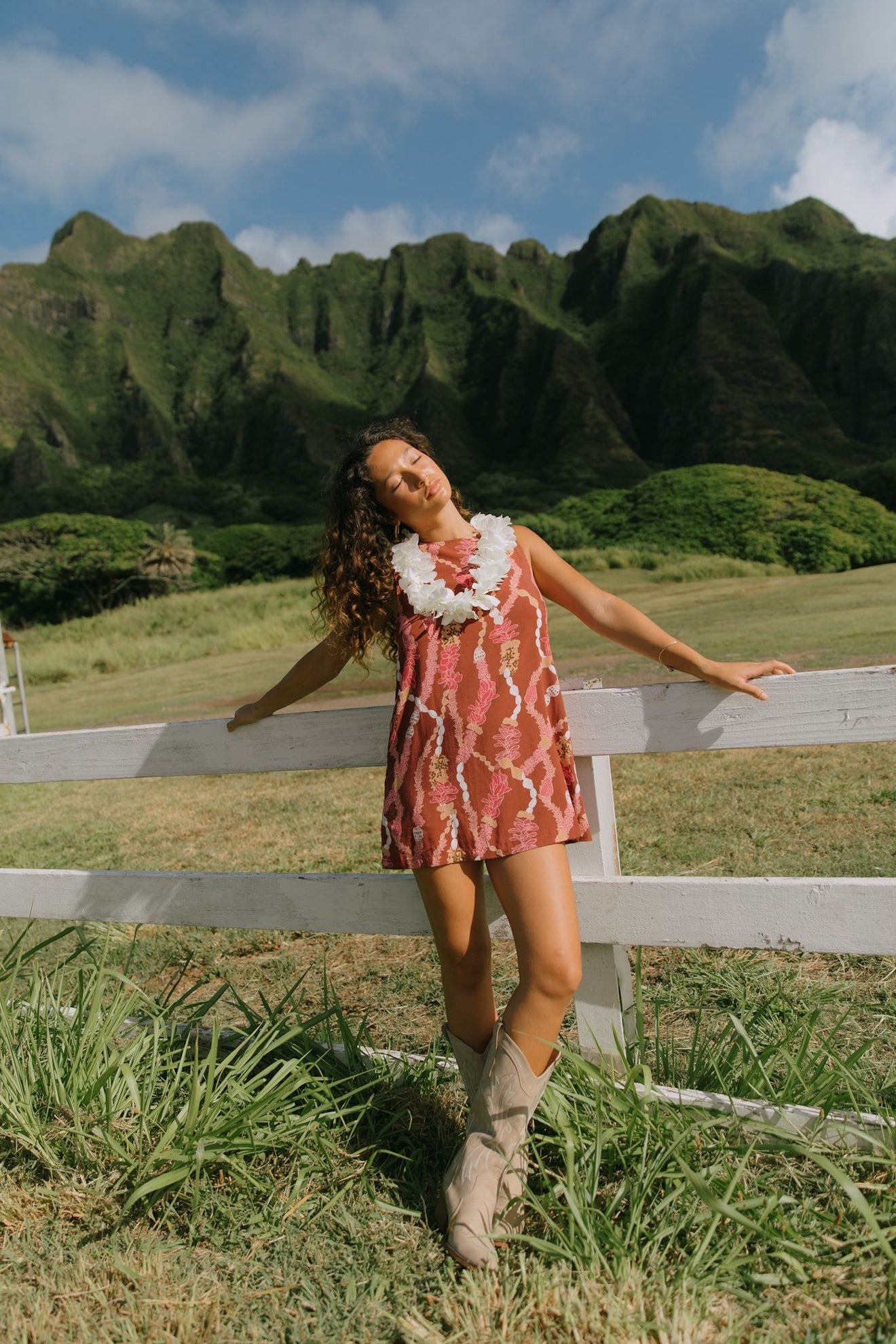 woman with brown hair wearing red-brown high neck scoop back dress with lei print