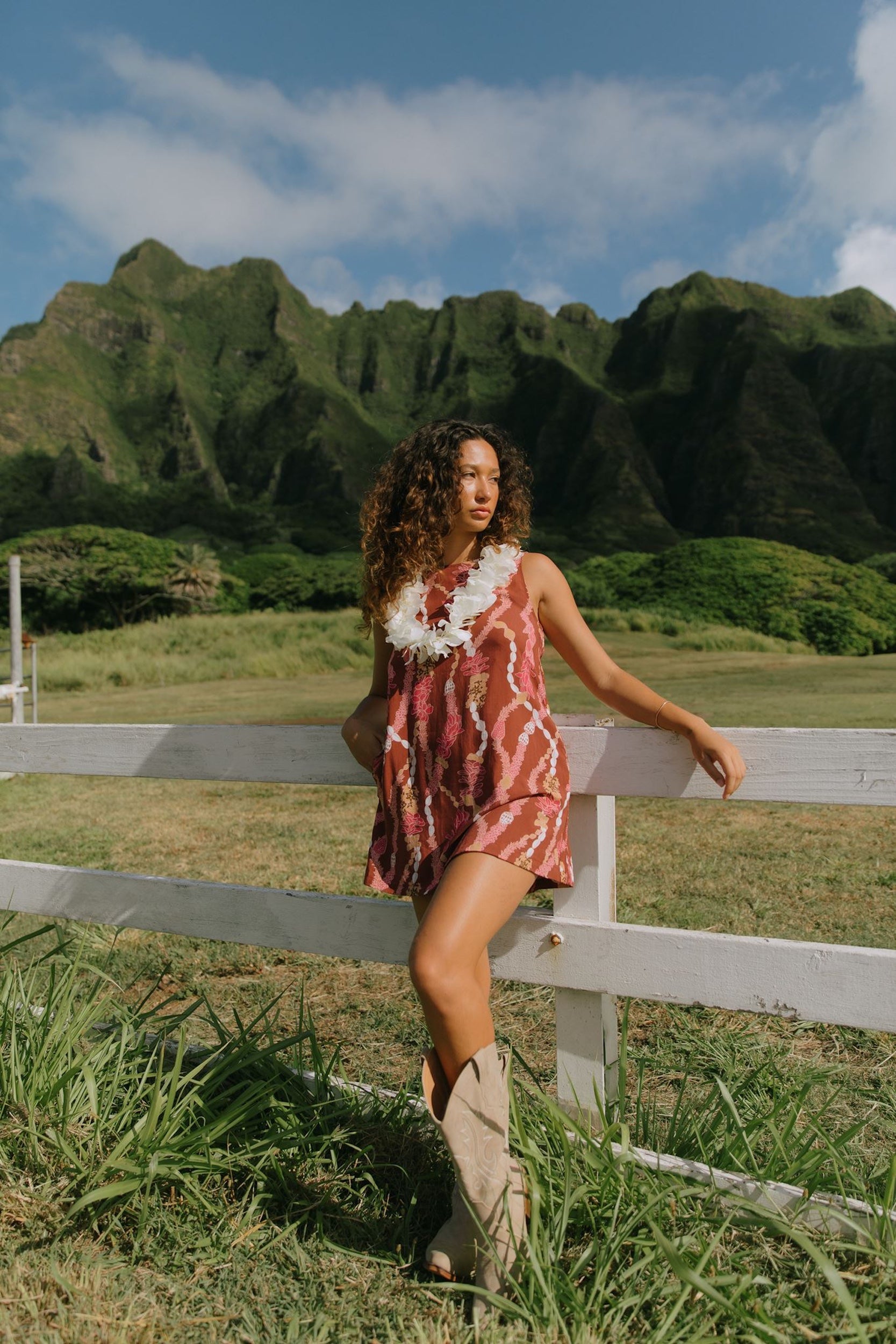 woman with brown hair wearing red-brown high neck scoop back dress with lei print