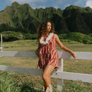 woman with brown hair wearing red-brown high neck scoop back dress with lei print