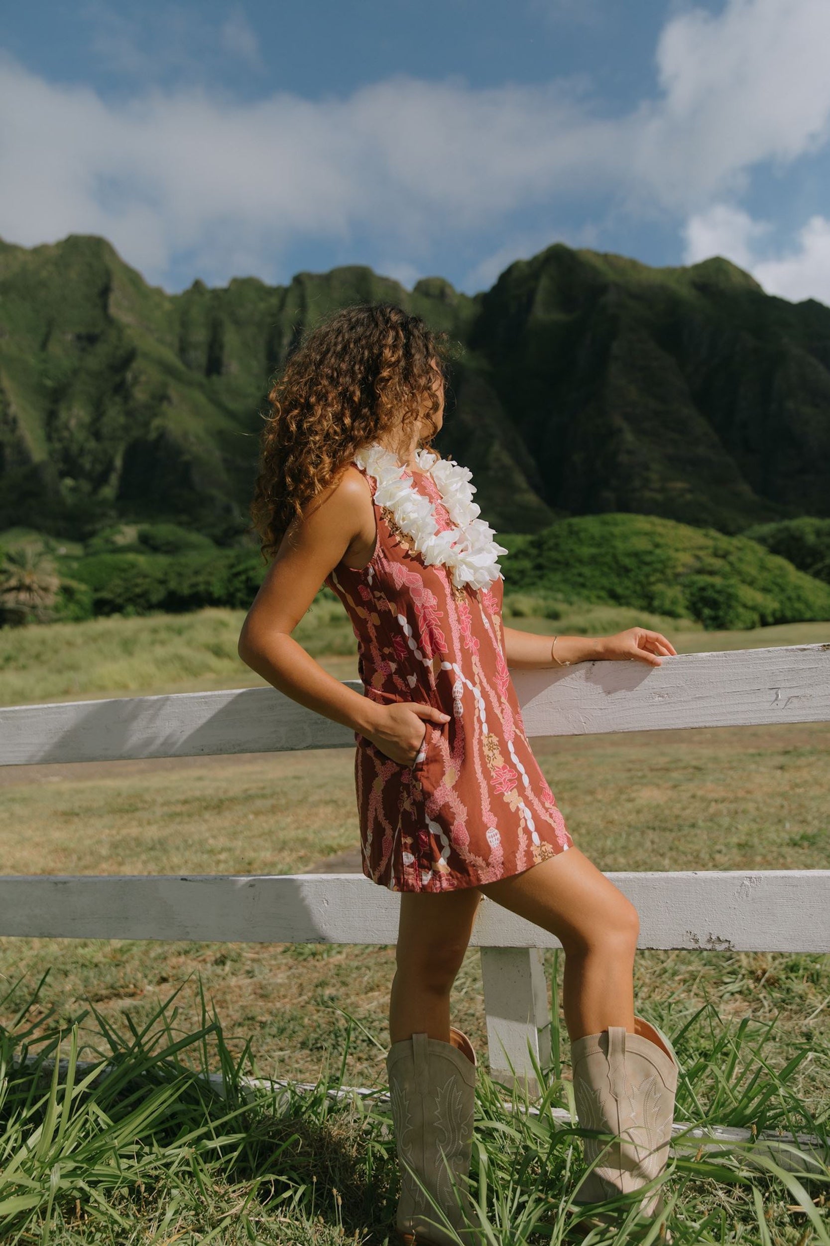 woman with brown hair wearing red-brown high neck scoop back dress with lei print