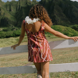 woman with brown hair wearing red-brown high neck scoop back dress with lei print