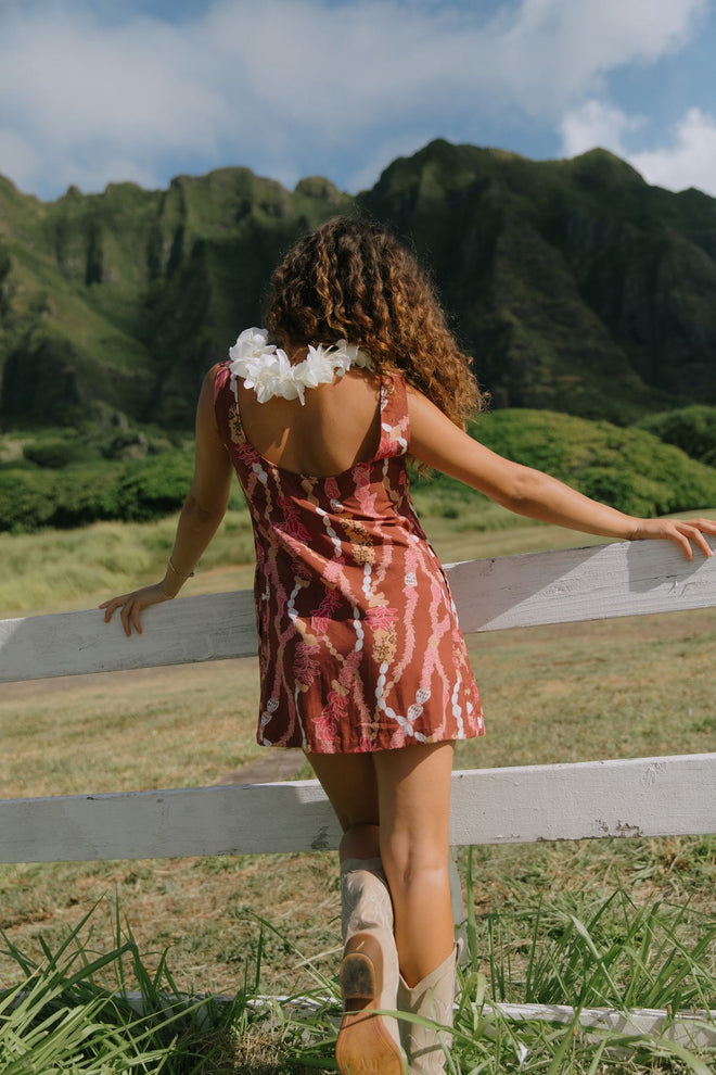 woman with brown hair wearing red-brown high neck scoop back dress with lei print