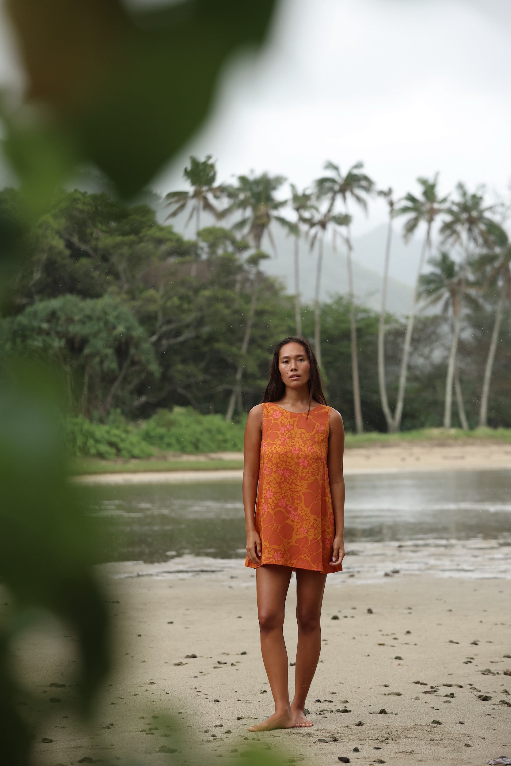 woman with brown hair wearing a retro orange mini scoop back dress with puakenikeni print