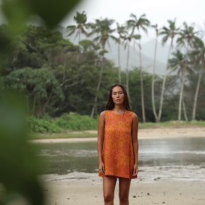 woman with brown hair wearing a retro orange mini scoop back dress with puakenikeni print