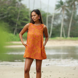 woman with brown hair wearing a retro orange mini scoop back dress with puakenikeni print
