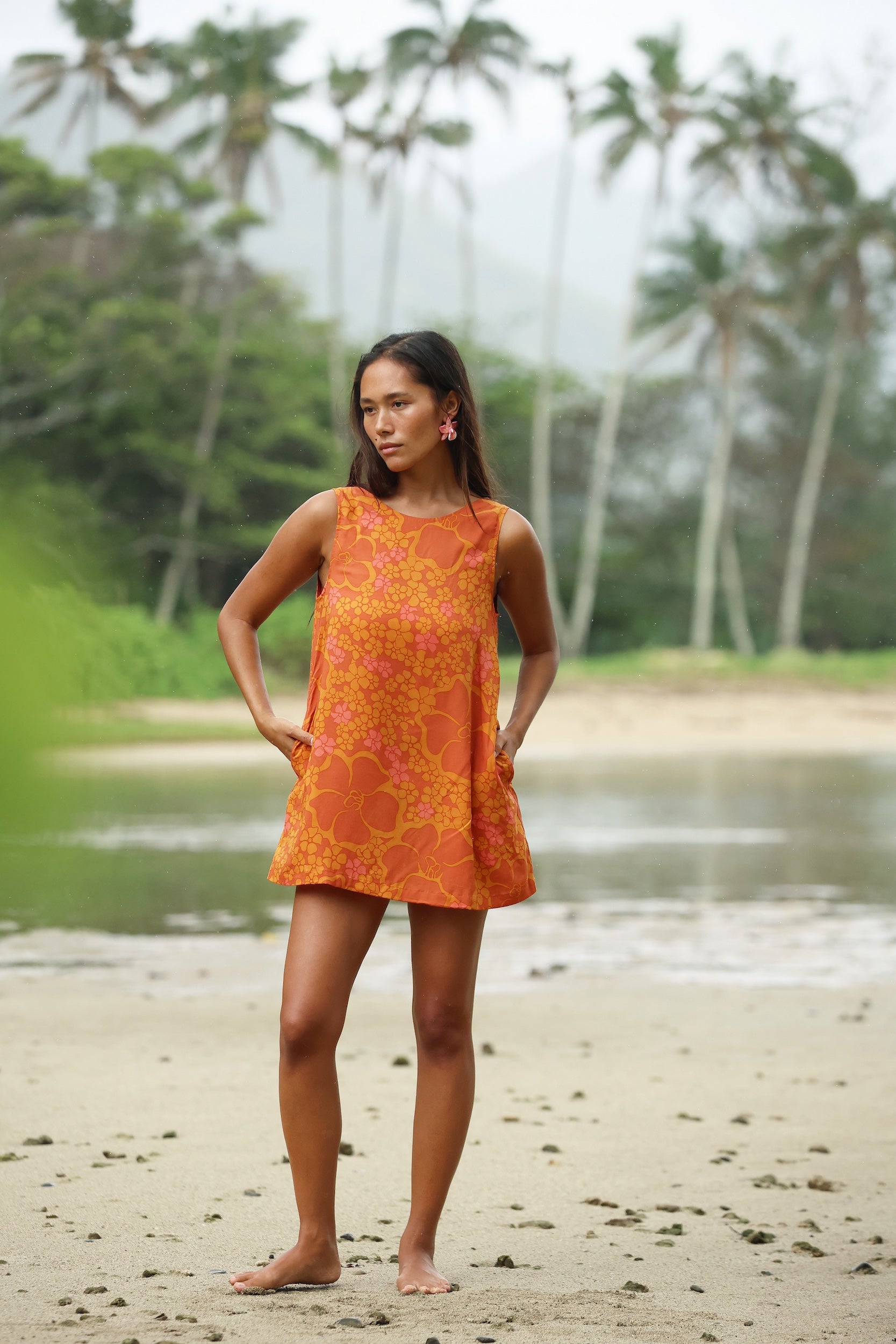 woman with brown hair wearing a retro orange mini scoop back dress with puakenikeni print