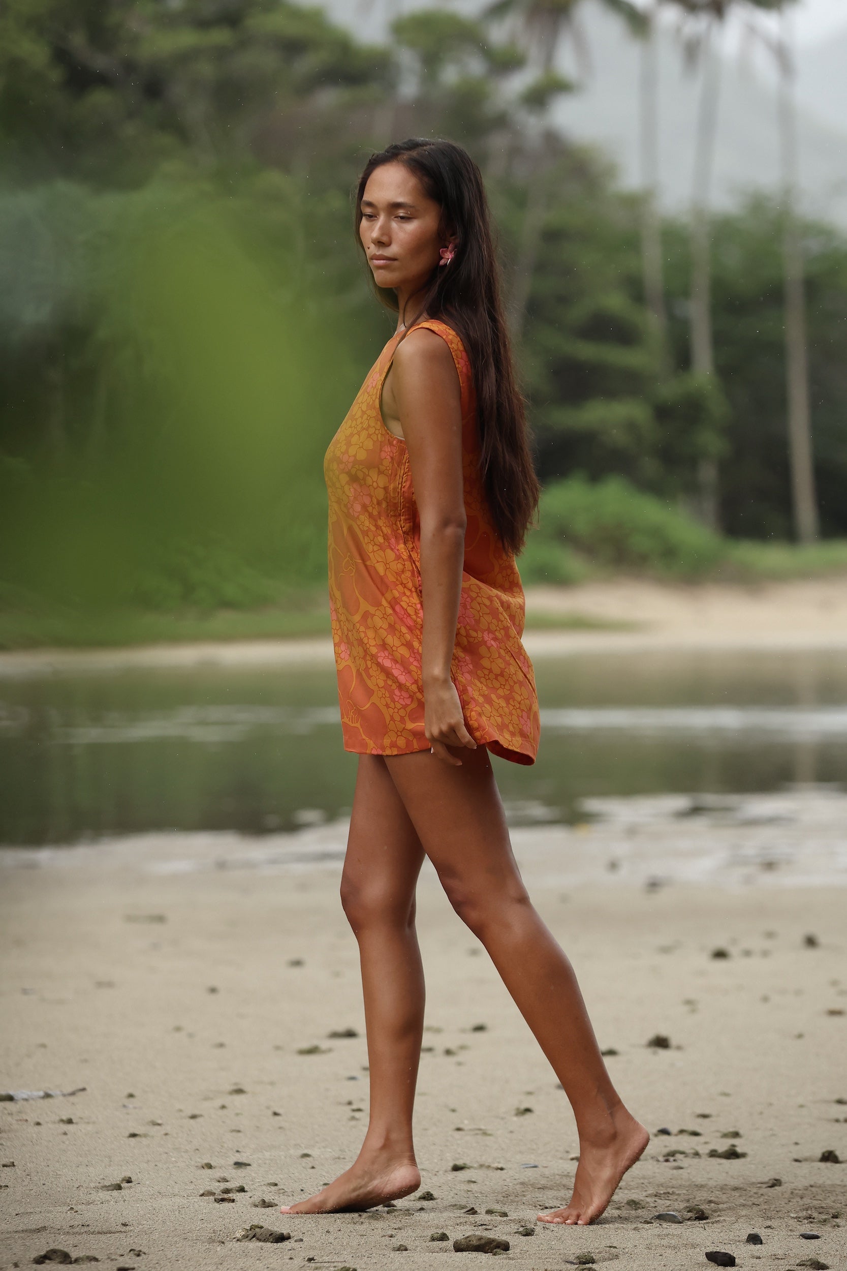 woman with brown hair wearing a retro orange mini scoop back dress with puakenikeni print