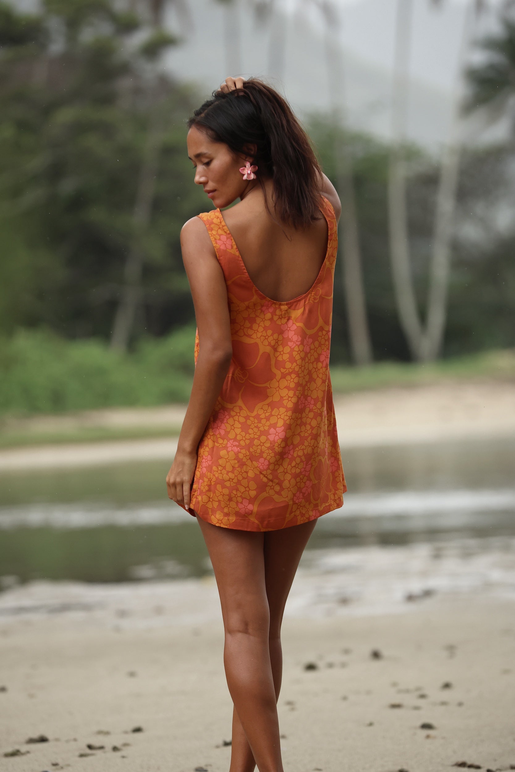 woman with brown hair wearing a retro orange mini scoop back dress with puakenikeni print