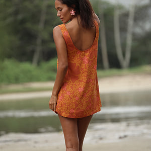 woman with brown hair wearing a retro orange mini scoop back dress with puakenikeni print