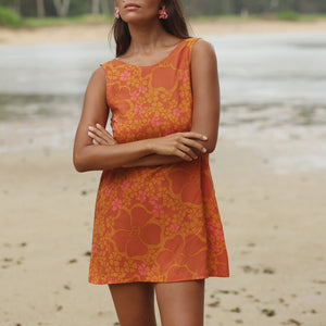 woman with brown hair wearing a retro orange mini scoop back dress with puakenikeni print