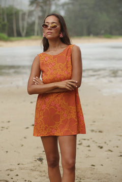woman with brown hair wearing a retro orange mini scoop back dress with puakenikeni print