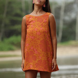 woman with brown hair wearing a retro orange mini scoop back dress with puakenikeni print