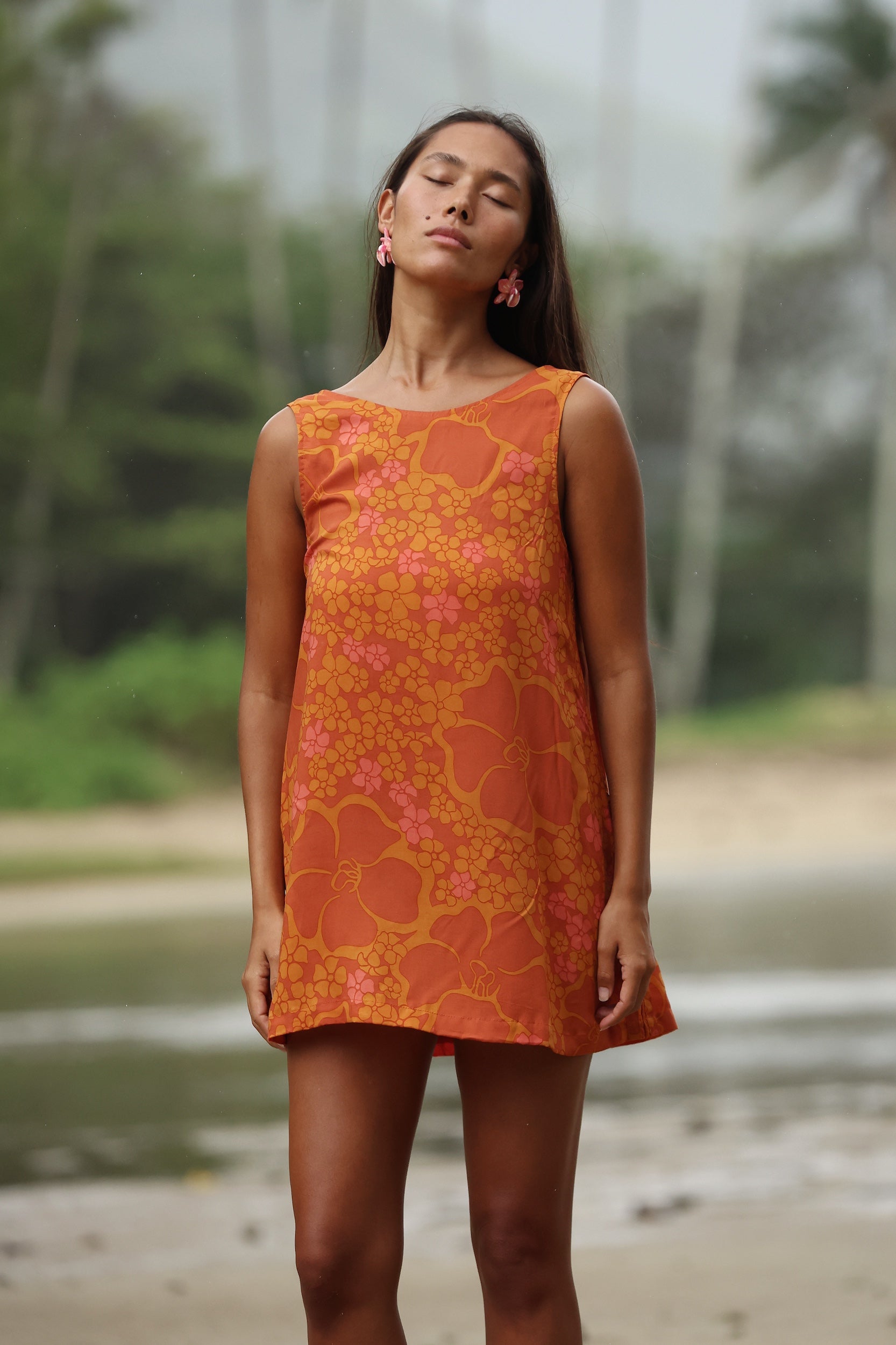 woman with brown hair wearing a retro orange mini scoop back dress with puakenikeni print