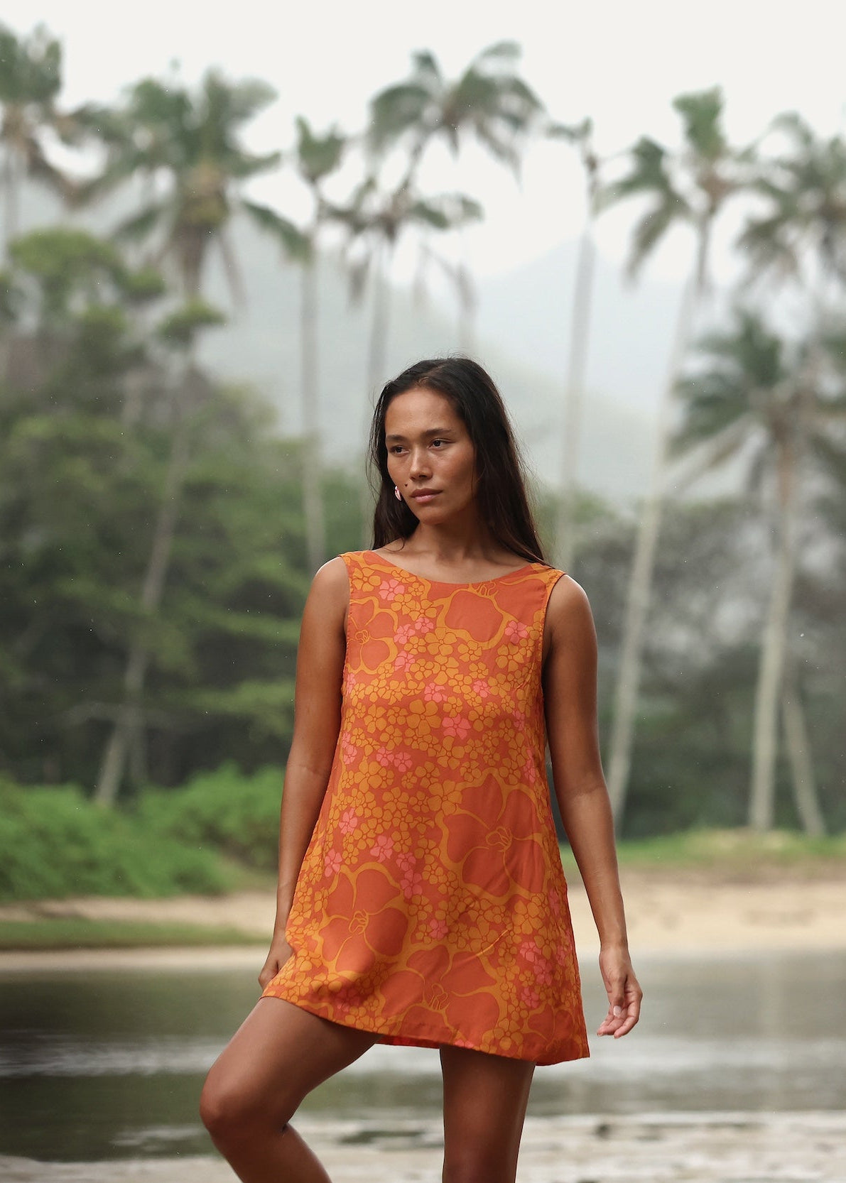 woman with brown hair wearing a retro orange mini scoop back dress with puakenikeni print