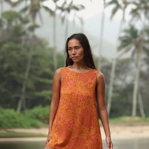 woman with brown hair wearing a retro orange mini scoop back dress with puakenikeni print