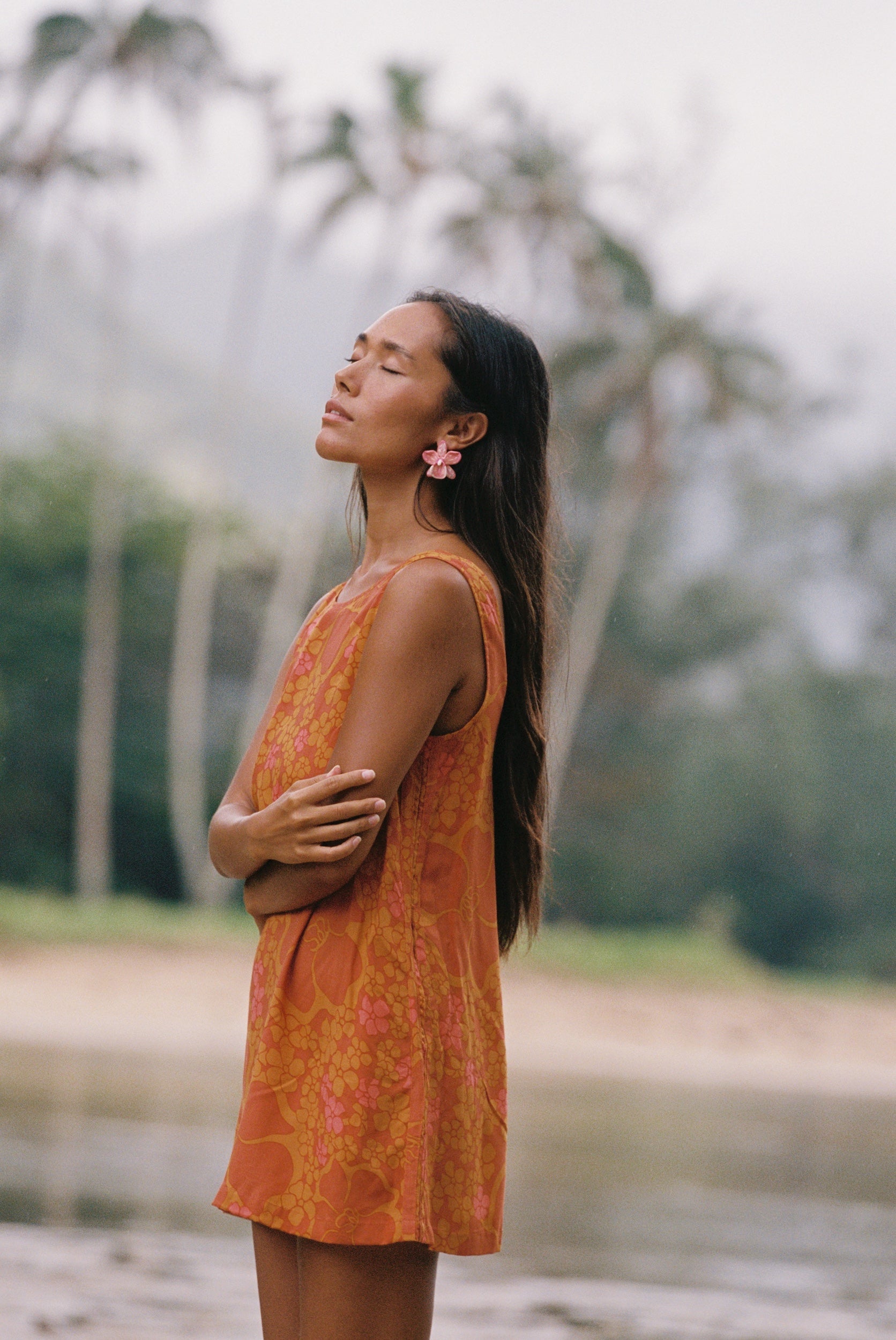 woman with brown hair wearing a retro orange mini scoop back dress with puakenikeni print