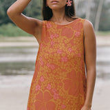 woman with brown hair wearing a retro orange mini scoop back dress with puakenikeni print