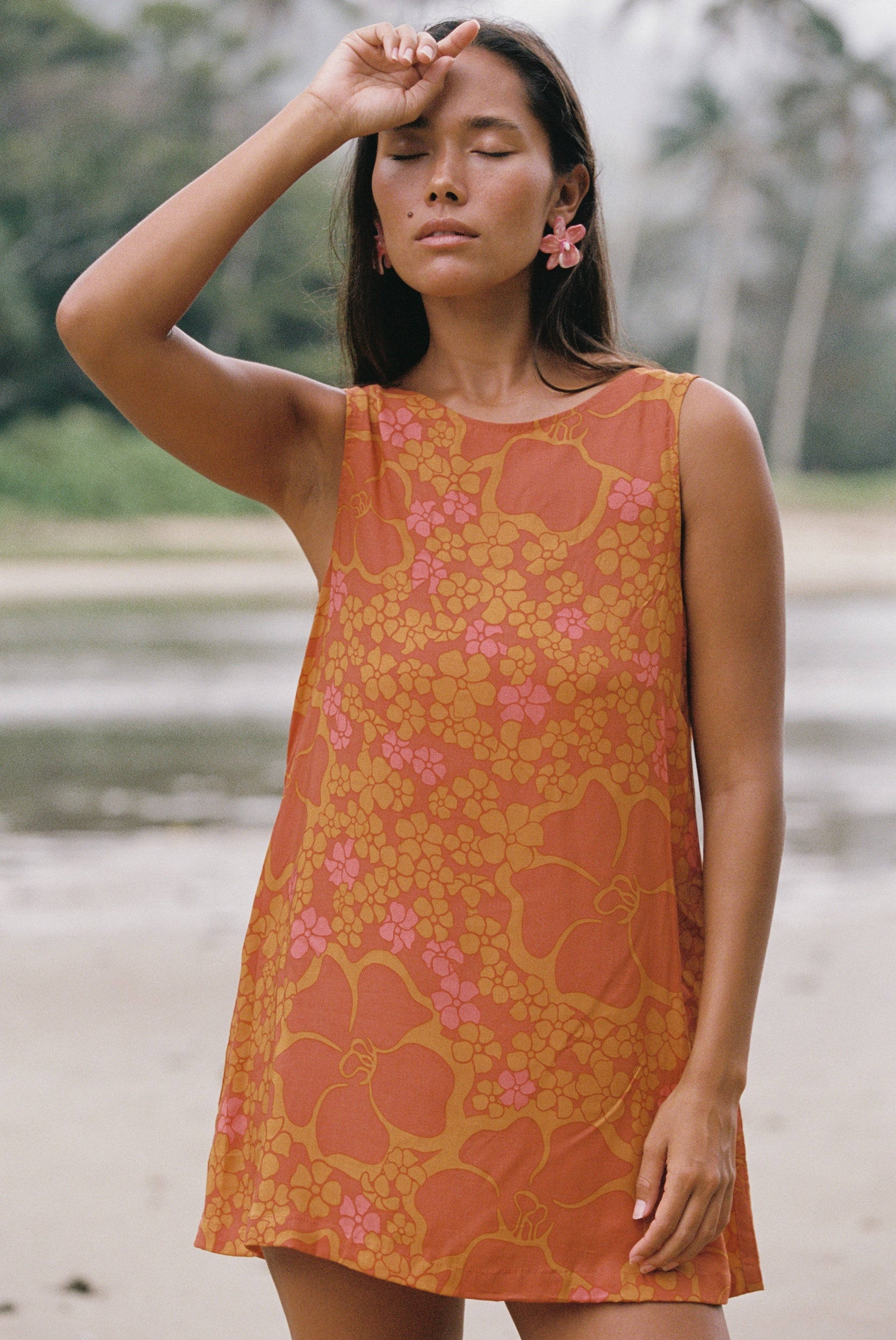 woman with brown hair wearing a retro orange mini scoop back dress with puakenikeni print