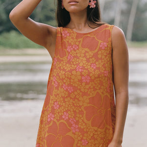 woman with brown hair wearing a retro orange mini scoop back dress with puakenikeni print
