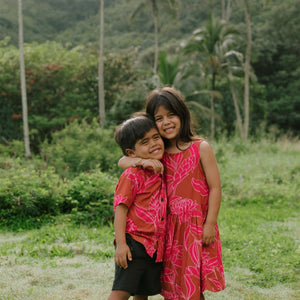 Boy in brown button up shirt with large pink floral print and girl in brown dress with large pink floral print
