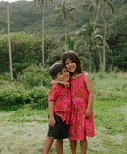 Boy in brown button up shirt with large pink floral print and girl in brown dress with large pink floral print