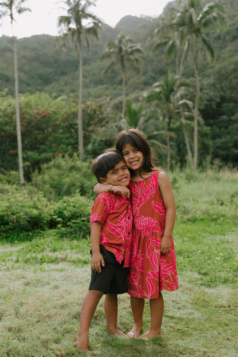 Boy in brown button up shirt with large pink floral print and girl in brown dress with large pink floral print