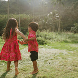 Boy in brown button up shirt with large pink floral print and girl in brown dress with large pink floral print