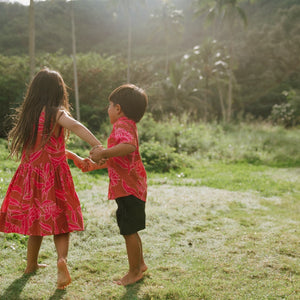 Boy in brown button up shirt with large pink floral print and girl in brown dress with large pink floral print