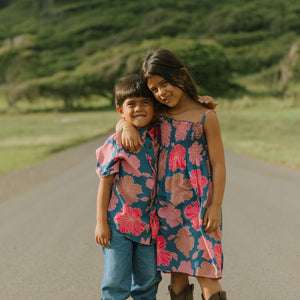 little girl wearing a navy spaghetti strap dress with bright pink hibiscus print