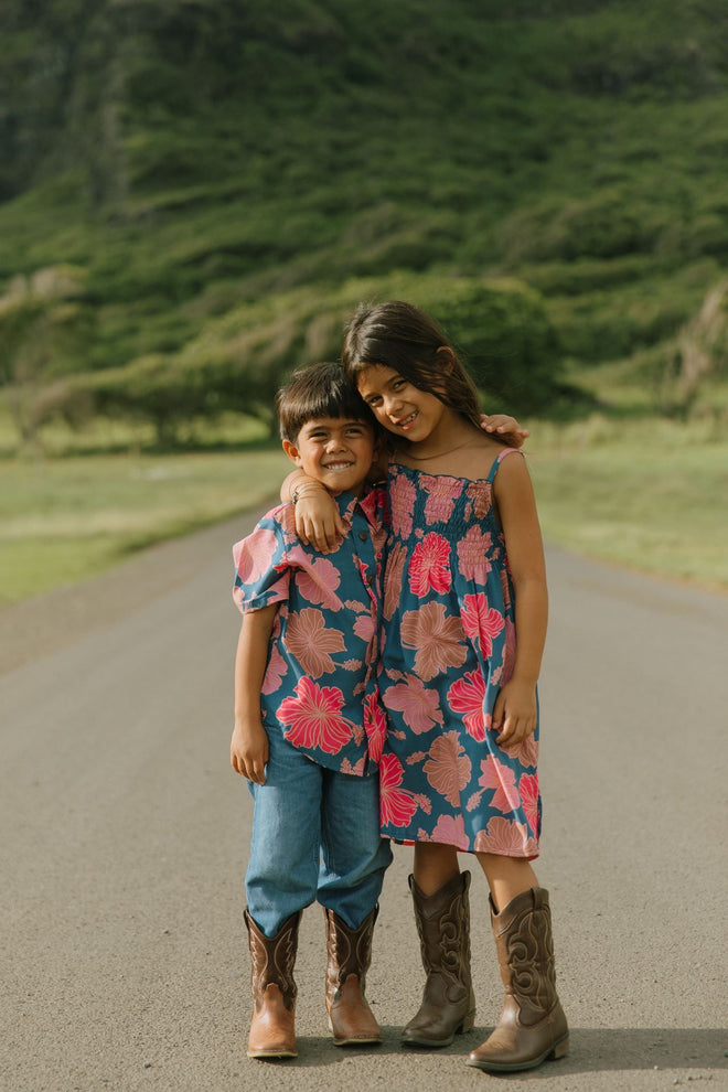 little girl wearing a navy spaghetti strap dress with bright pink hibiscus print