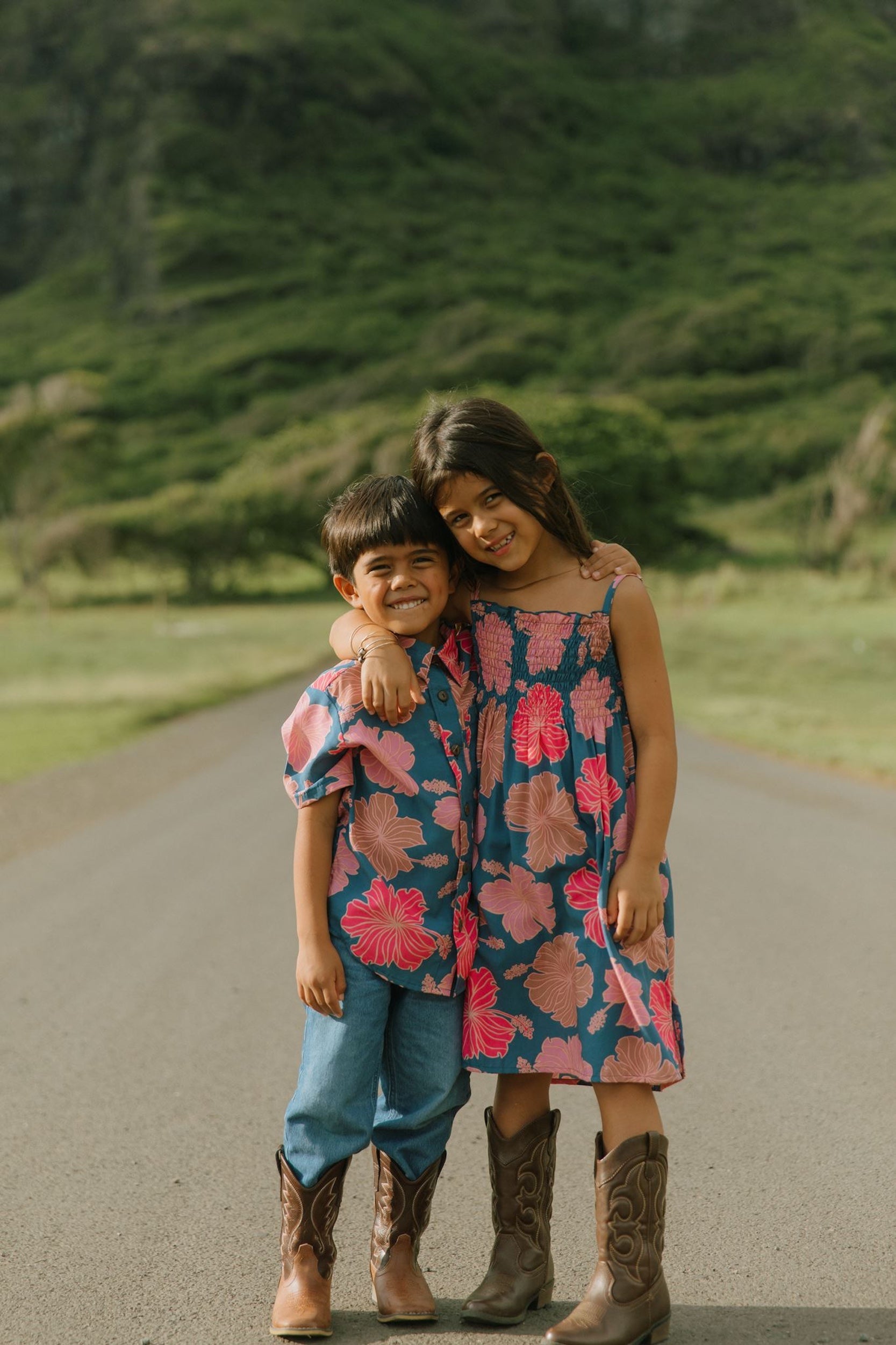 little boy wearing a nevy button up aloha shirt with bright pink hibiscus print