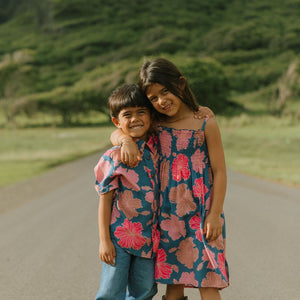 little boy wearing a nevy button up aloha shirt with bright pink hibiscus print