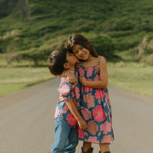 little girl wearing a navy spaghetti strap dress with bright pink hibiscus print