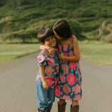 little boy wearing a nevy button up aloha shirt with bright pink hibiscus print