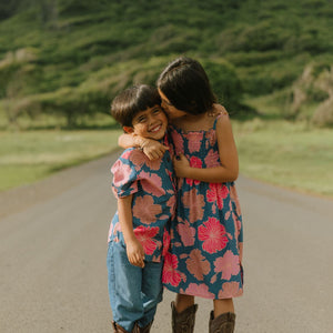 little boy wearing a nevy button up aloha shirt with bright pink hibiscus print
