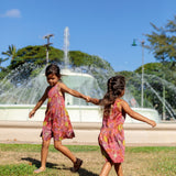 little girl wearing terracotta colored high neck sleeveless knee length dress with large purple and yellow flower print