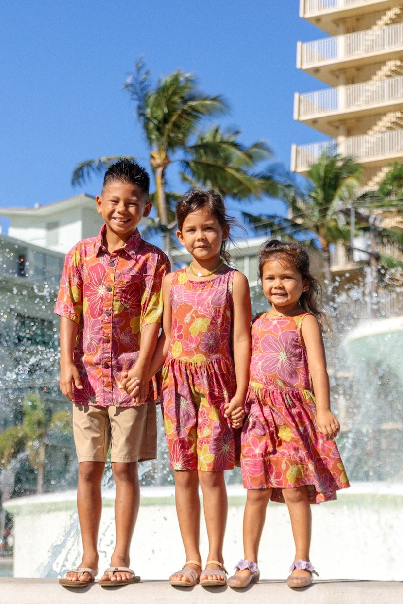 little boy wearing terracotta colored aloha shirt with large purple and yellow flower print 