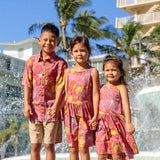 little boy wearing terracotta colored aloha shirt with large purple and yellow flower print 