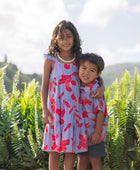 little boy with brown hair wearing a button up aloha shirt with periwinkle background and bright red hibiscus print.
