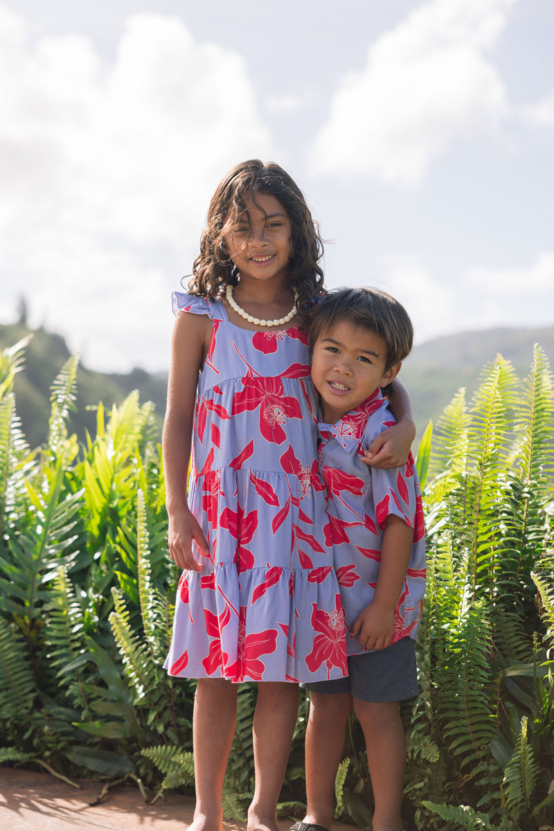 little boy with brown hair wearing a button up aloha shirt with periwinkle background and bright red hibiscus print.