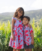 little girl with brown hair wearing a mid length dress with periwinkle background and bright red hibiscus print.