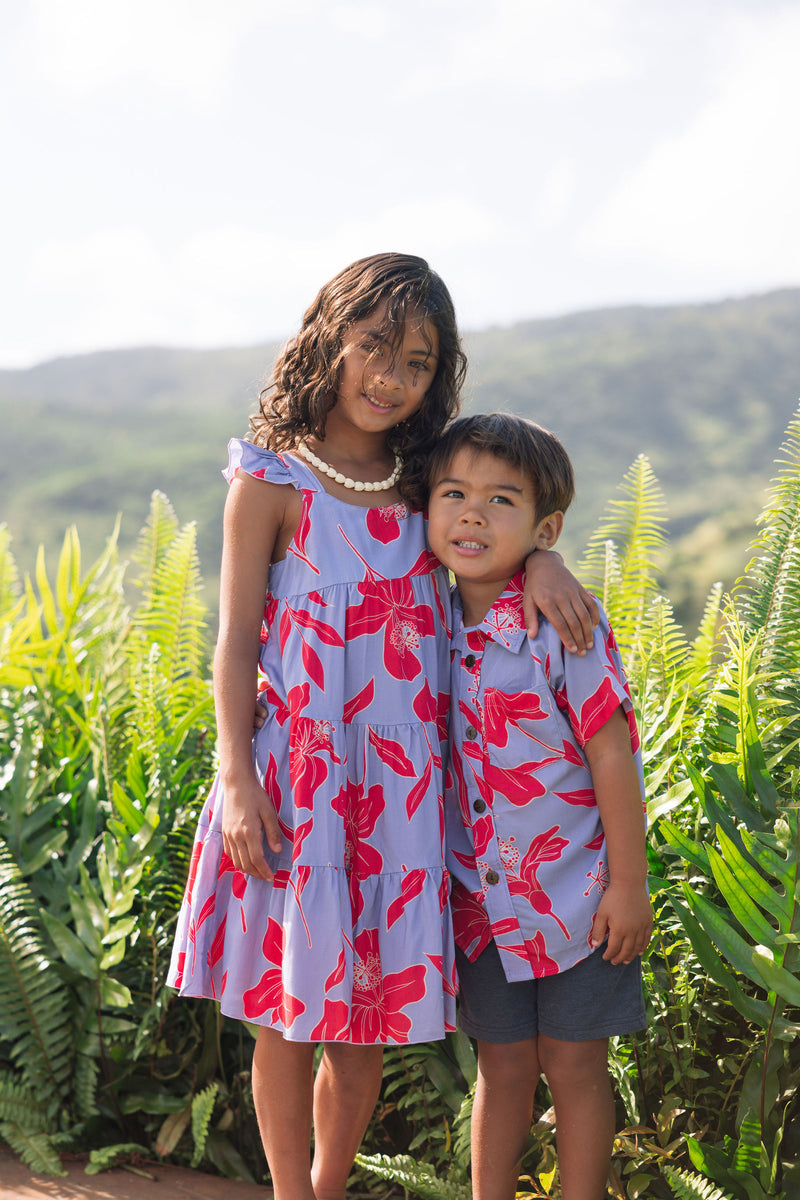 little girl with brown hair wearing a mid length dress with periwinkle background and bright red hibiscus print.