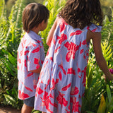 little boy with brown hair wearing a button up aloha shirt with periwinkle background and bright red hibiscus print.