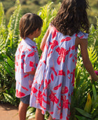 little boy with brown hair wearing a button up aloha shirt with periwinkle background and bright red hibiscus print.