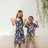 little boy wearing button up aloha shirt in navy and pink hibiscus print.